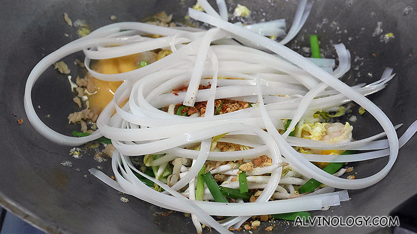 Putting all the pad thai ingredients into the wok
